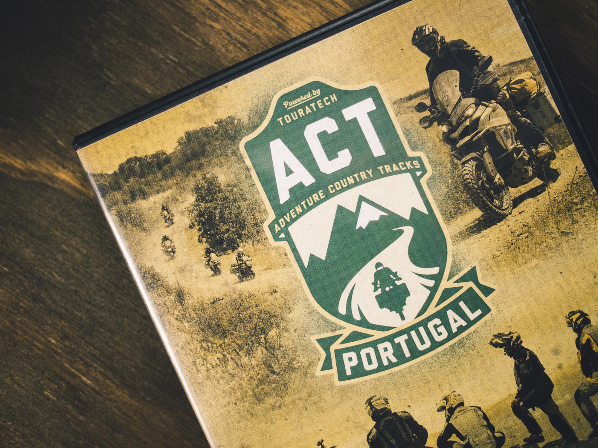 Man sieht das Foto einer DVD-Hülle der Adventure Country Tracks Portugal von TOURATECH. Der Focus liegt auf dem ACT-Logo, darunter sieht man Motorrad-Fahrer im Gelände. Das Corporate Design ist von MAJORMAJOR.
