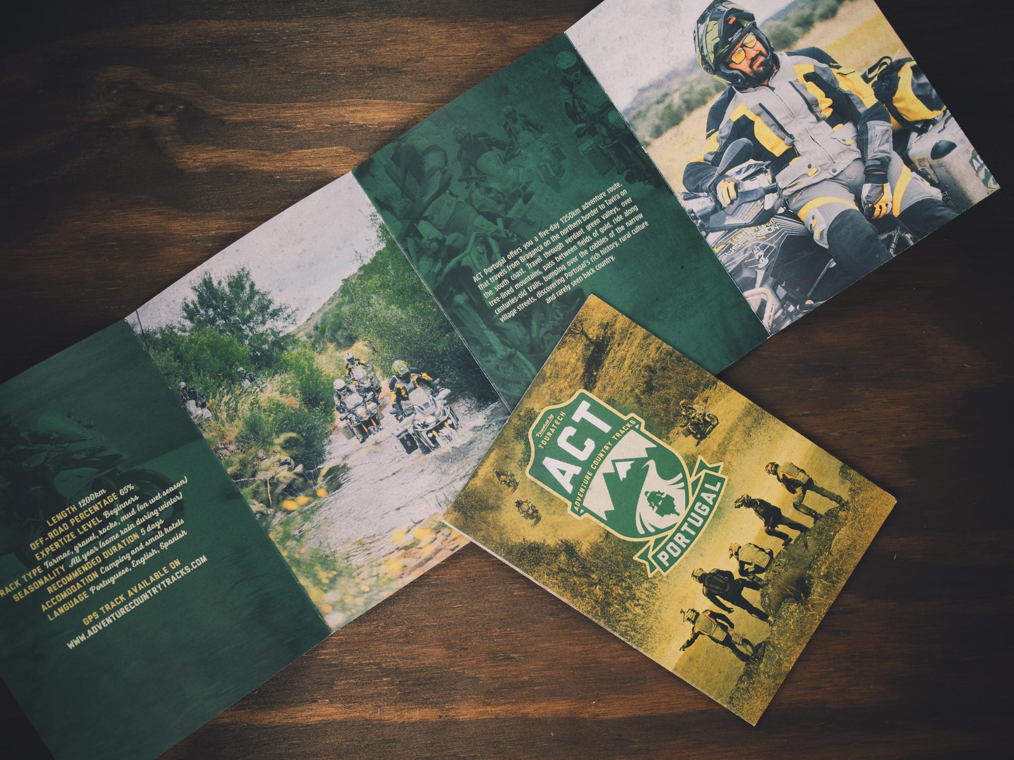 Man sieht das Foto des Begleitheftes der Adventure Country Tracks-DVD von TOURATECH. Die Vorderseite dominiert das ACT-Logo, im Innenteil sieht man Motorrad-Fahrer bei Wasserdurchfahrt. Das Corporate Design ist von MAJORMAJOR.
