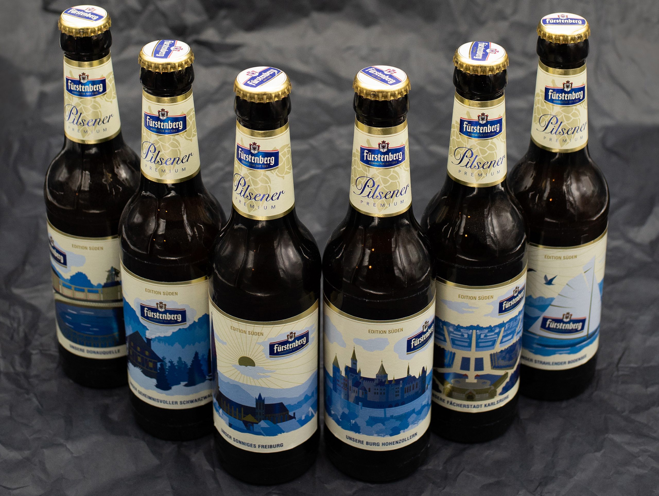 Man sieht alle sechs Bierflaschen der Designedition Süden der Fürstlich Fürstenbergischen Brauerei aus dem Jahr 2019. Mittig ist das Freiburger Münster und die Burg Hohenzollern auf den Etiketten zu sehen. Das Design ist von MAJORMAJOR.